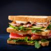Grote Club Sandwich Met Ham, Spek, Tomaat, Komkommer, Kaas, Eieren En Kruiden Op Donkere Achtergrond