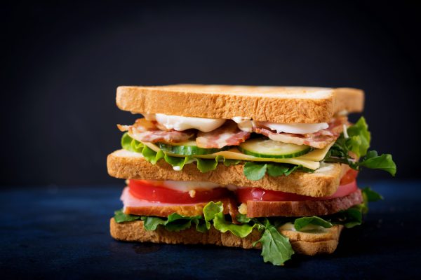 Grote Club sandwich met ham, spek, tomaat, komkommer, kaas, eieren en kruiden op donkere achtergrond