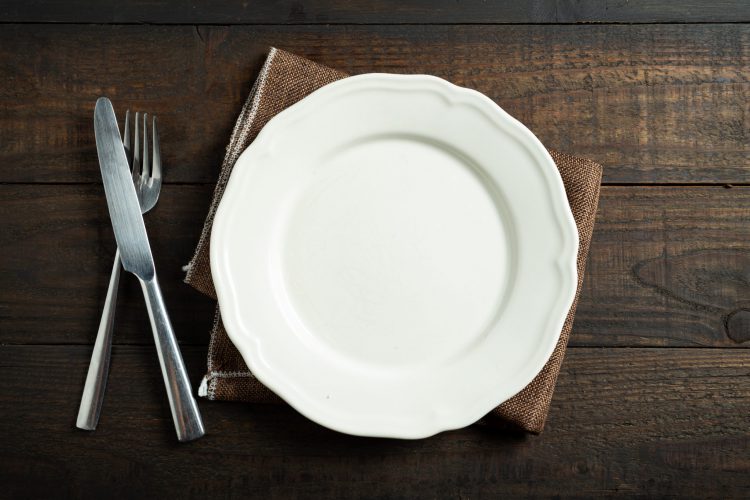 Leeg wit bord op houten tafel met bestek.