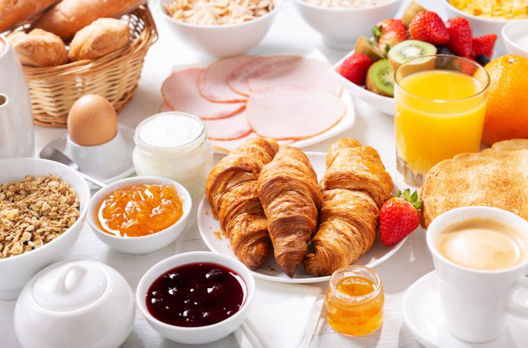 Ontbijt met croissants, koffie, sap, vlees, jam, granen en vers fruit op een houten tafel