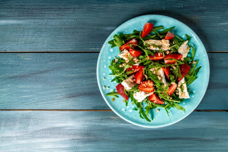 Salade met rucola, aardbeien en kaas brie, camembert. Lange banner formaat. ruimte voor tekst. Vanaf bovenaanzicht gefotografeerd.