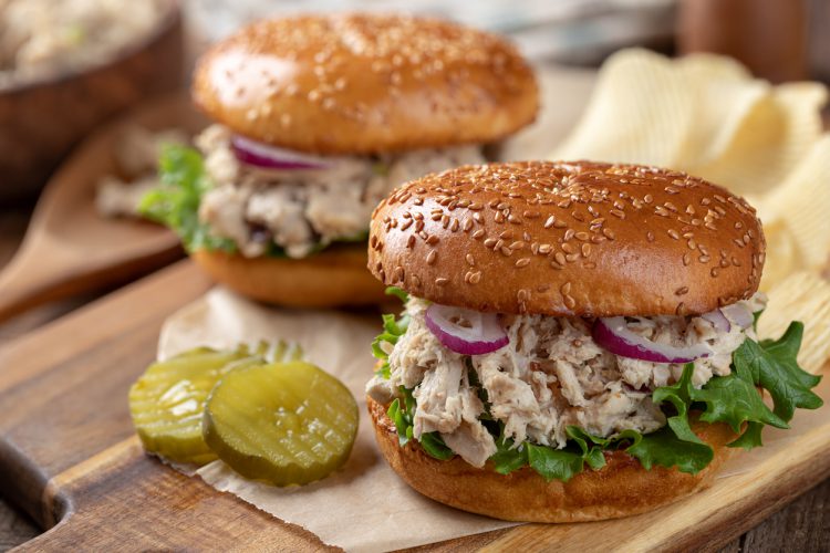 Broodje tonijnsalade en sla op geroosterd sesamzaadbroodje met augurken en aardappelchips op houten snijplank