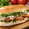 Submarine Sandwich Gemaakt Met Kalkoen, Ham, Kaas Sla En Tomaat Op Een Hoagie Broodje Met Sla En Tomaten Op De Achtergrond.