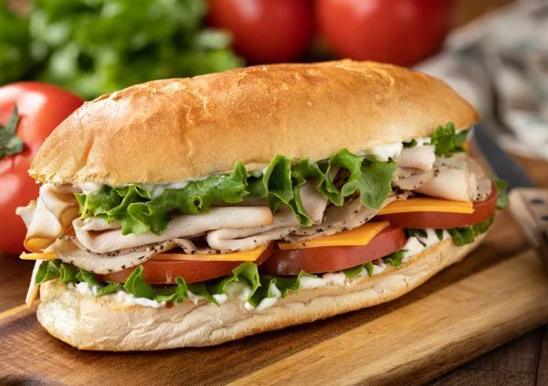 Zacht broodje Submarine sandwich gemaakt met kalkoen, ham, kaas sla en tomaat op een hoagie broodje met sla en tomaten op de achtergrond.