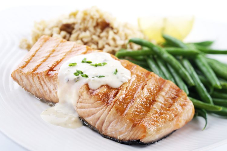 Zalm steak met een lichte saus, groene bonen, en bruine rijst pilaf voor een gezond diner.