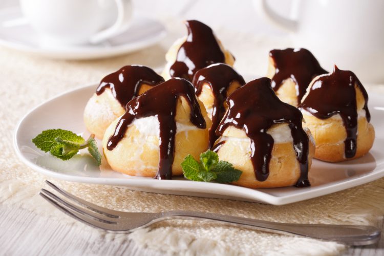 Heerlijke eclairs met room en chocolade glazuur op een bord. Foto horizontaal gefotografeerd.