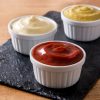 Ketchup, Mosterd En Mayonaise In Witte Kommetjes Op Een Zwarte Slat.