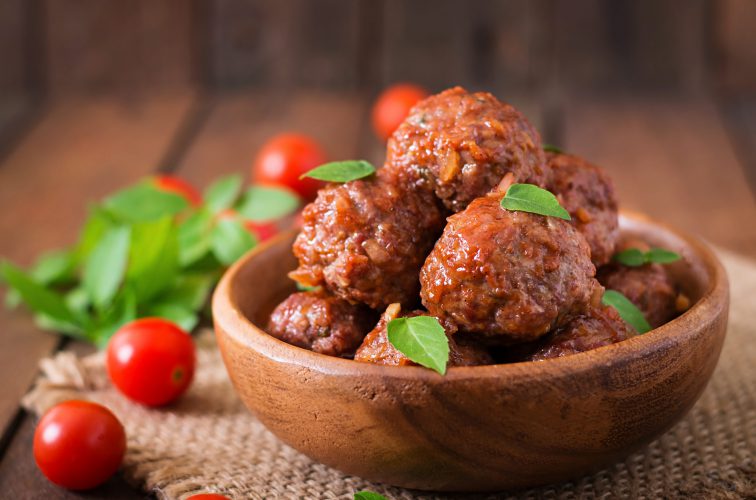 Gehaktballen in zoetzure tomatensaus en basilicum in een houten kom.