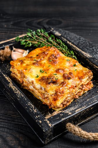 Portie lasagne met gehakt en tomaten bolognese-saus geserveerd in een houten schaal.