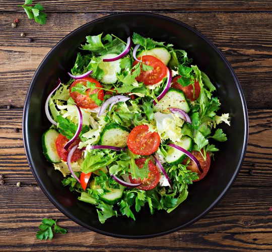 Salade van tomaten, komkommer, rode uien en sla. Gezond zomer vitamine menu. Veganistisch plantaardig voedsel. Vegetarische eettafel. Bovenaanzicht.