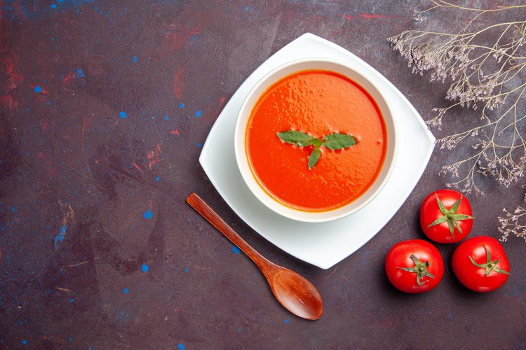 Heerlijke tomatensoep, een lekkere smakelijke schotel met rucola binnen plaat op donkere achtergrond.