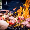 Gedetailleerde Foto Van Rundvleesburgers, Worsten En Twee Spiesjes Op De Barbecue Waar Ook Vlammen Bij Te Zien Zijn.