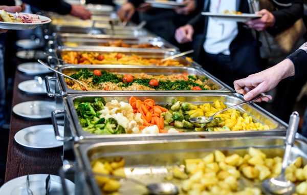 Groep mensen die een all you can eat catering buffet eten binnen in luxe restaurant waarbij vlees en groenten uit buffetbakken wordt opgeschept.